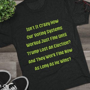 Op de afbeelding: Donkergrijs t-shirt met de tekst "Isn't It Crazy How Our Voting Systems Worked Just Fine Until Trump Lost An Election? And They Work Fine Now As Long As He Wins?" in het groen.