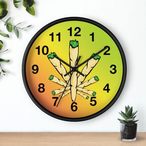May include: A round wall clock with a black frame. The clock face features a cannabis leaf design made of rolled joints against a gradient background of yellow and orange. Black hands indicate the time.