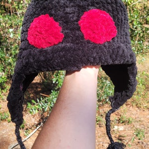 May include: Black crocheted hat with red fuzzy pom-poms. The hat has long ear flaps and a braided tassel.