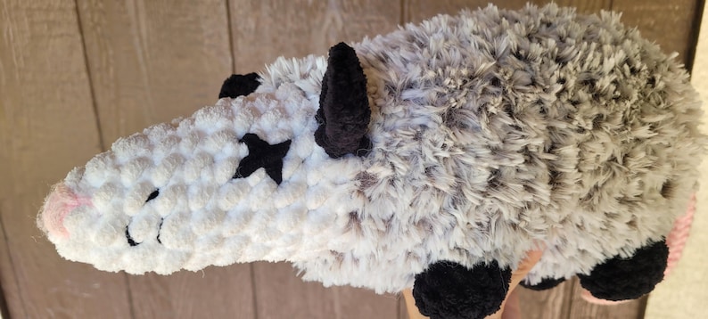 Puede incluir: Un juguete de peluche de zarig&uuml;eya hecho a mano. La zarig&uuml;eya es principalmente gris y blanca con detalles en negro para las orejas, los pies y los ojos. La nariz es rosa. Los ojos son cruces negras. La cola es rosa.