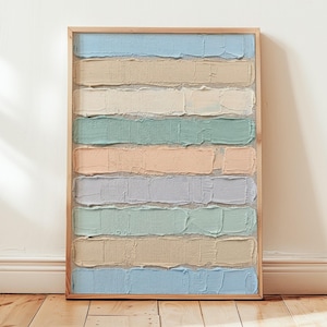 May include: A framed abstract artwork featuring horizontal bands of textured paint in pastel colors. The colors include light blue, beige, white, green, peach, and lavender. The artwork is displayed against a white wall and wooden floor.