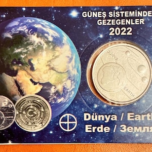 May include: A commemorative coin set featuring a depiction of Earth and the solar system. The packaging includes the text "GÜNEŞ SİSTEMİNDEKİ GEZEGENLER 2022" and the words "Dünya / Earth". The coins are silver-colored and set against a blue and purple background.
