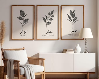 May include: Three framed art prints with botanical illustrations and inspirational words. Each print features a black and white leaf design with the words "Trust", "Gratitude", and "Patience" in both English and Arabic script. The frames are a light brown color.