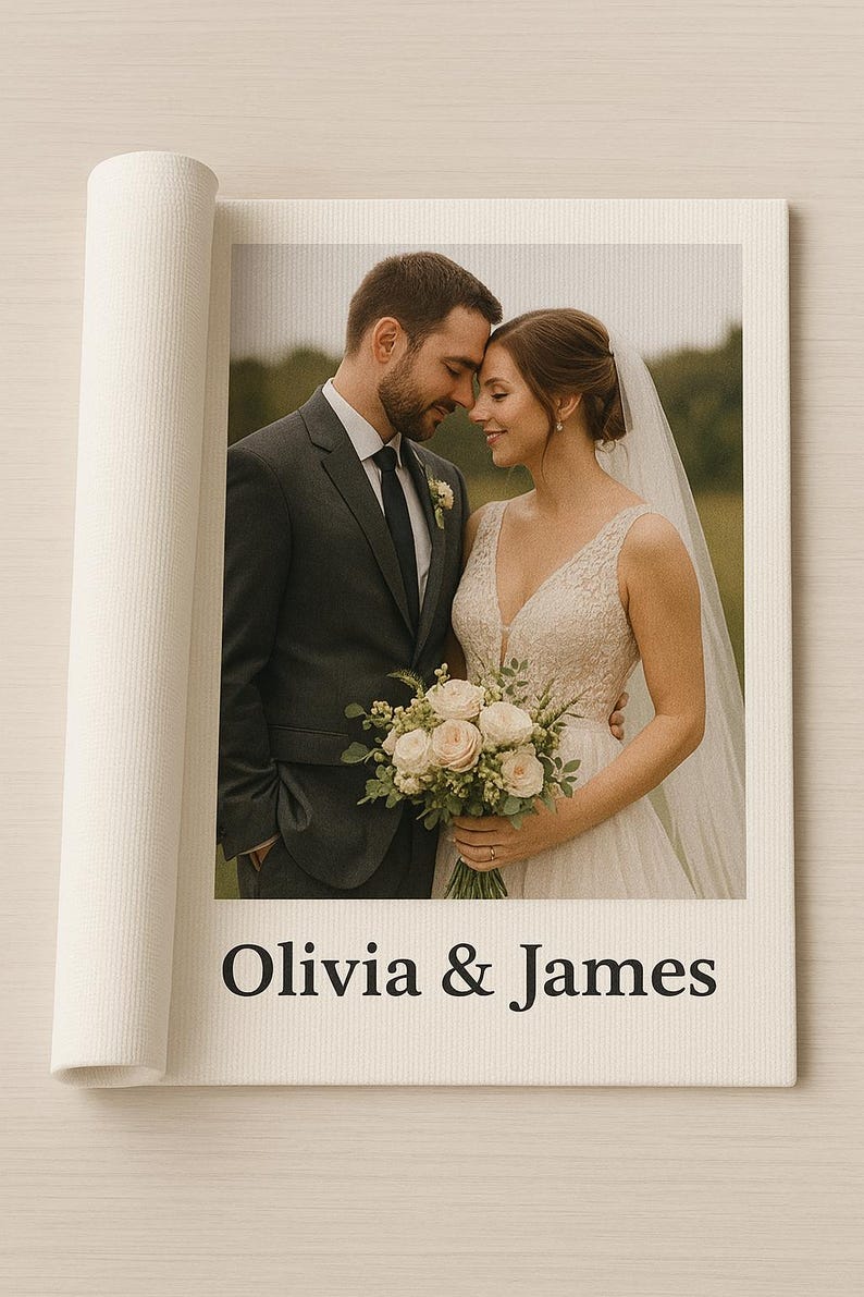 K&ouml;nnte beinhalten: Ein rechteckiger Leinwanddruck mit einem Foto eines Paares in Hochzeitskleidung, wobei der Text Olivia & James in Schwarz unter dem Bild gedruckt ist. Die Leinwand hat eine gerollte Kante auf der linken Seite und eine strukturierte, cremewei&szlig;e Oberfl&auml;che.