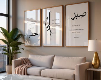 May include: Three framed art prints with gold frames hang above a beige sofa. The prints feature black calligraphy and English text on a white background. The first print says "LOVE", the second "GRATITUDE", and the third "PATIENCE". A large plant and a lamp are also visible.