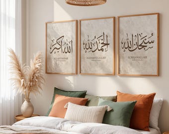 May include: Three framed wall art pieces with Arabic calligraphy in brown script. The art is displayed above a bed with decorative pillows in shades of green, orange, and cream. A woven pendant light hangs from the ceiling.