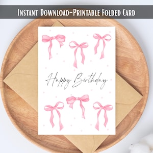 May include: A birthday card with a watercolour design of pink bows and the words "Happy Birthday" in script. The card is presented with a brown envelope on a wooden tray. The text "INSTANT DOWNLOAD-PRINTABLE FOLDED CARD" is at the top of the card.