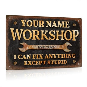 Puede incluir: Un letrero metálico rectangular con un aspecto desgastado y oxidado. El letrero presenta las palabras "YOUR NAME WORKSHOP" en letras doradas, con un gráfico de llave inglesa y el texto "I CAN FIX ANYTHING EXCEPT STUPID."
