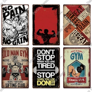 May include: Collection of six metal signs with gym-themed designs. The signs feature motivational quotes, illustrations of weightlifters, and the words "No Pain No Gain," "Old Man Gym," and "Fitness Gym." The signs are rectangular and have a vintage aesthetic.