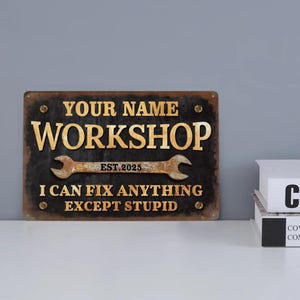 Puede incluir: Un letrero de metal oxidado con el texto "YOUR NAME WORKSHOP EST. 2025 I CAN FIX ANYTHING EXCEPT STUPID". El letrero tiene un diseño de llave inglesa y es negro con letras doradas.