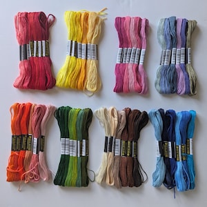 May include: A selection of embroidery threads in a spectrum of colours, such as red, yellow, pink, blue, orange, green, and brown. Each bundle is neatly wrapped and labelled, displaying a variety of shades for craft projects.