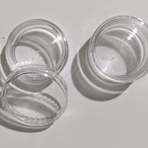 May include: Two clear plastic containers with lids. The containers are round and have a smooth, shiny finish.