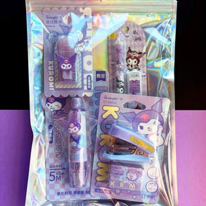 May include: A clear, holographic zip bag containing several purple and white Kuromi-themed stationery items. The items include a stapler, tape dispenser, eraser, and pens. The packaging features cartoon character illustrations and Chinese text.