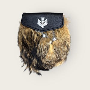 May include: A traditional Scottish kilt sporran with a black leather top and a fur body. The sporran features a silver thistle emblem and two decorative tassels. The fur is a mix of brown and black.