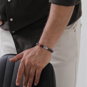 May include: A beaded bracelet featuring a variety of colorful gemstones and dark gray beads. The bracelet is worn on a wrist, showcasing the different colors and textures of the stones. The bracelet is a piece of jewelry.