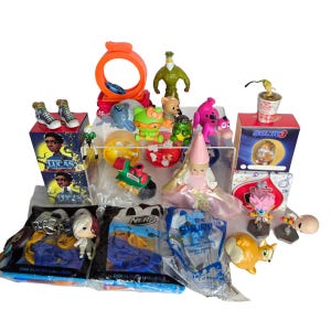 Peut inclure: Une collection de jouets et figurines en plastique assortis comprenant une boîte Sonic 3, une boîte Lucas, un chien rose, une tortue verte, une poupée en robe rose, des emballages Nerf disk blaster challenge et diverses petites figurines sur fond blanc.