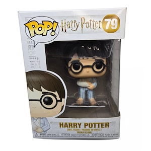 May include: A Harry Potter vinyl figure in a display box. The figure is of Harry Potter wearing glasses and pajamas, with a bandaged arm. The box has the Pop! logo and the text "Harry Potter 79".