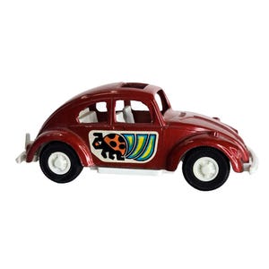 May include: A red toy car with white wheels and a black tire. The car has a sunroof and a sticker with a ladybug and colorful stripes. The car is a vintage style toy.