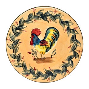 May include: A ceramic plate with a hand-painted design of a rooster with a yellow, blue, and red plumage standing on a branch surrounded by green leaves. The plate has a light orange background.
