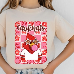 natural t-shirt featuring a cartoon cardinal with star-shaped sunglasses blowing a bubble. The cardinal is wearing a white shirt with red stripes. The word "Cardinals" is written in brown script within a pink and red floral frame.