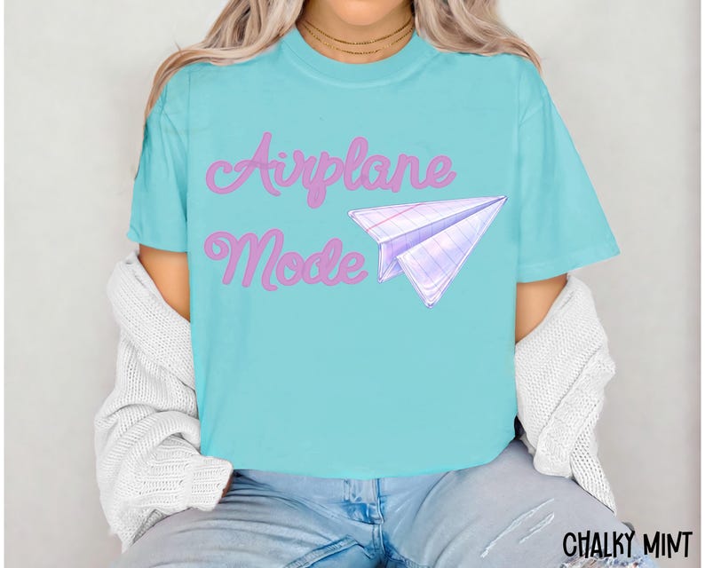 A turquoise t-shirt with the words "Airplane Mode" in pink script and a paper airplane graphic. The shirt is a short-sleeved, casual style.