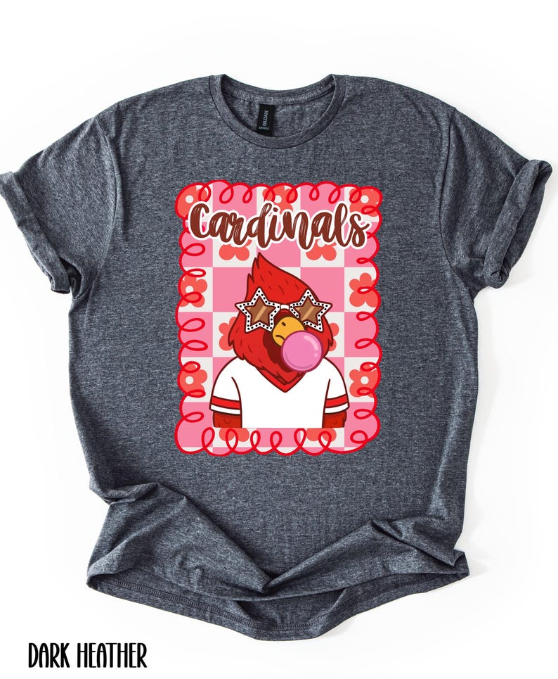 Dark heather gray t-shirt featuring a cartoon cardinal wearing star-shaped sunglasses and blowing a bubblegum bubble. The shirt has the word "Cardinals" in a decorative font within a pink and red floral frame.
