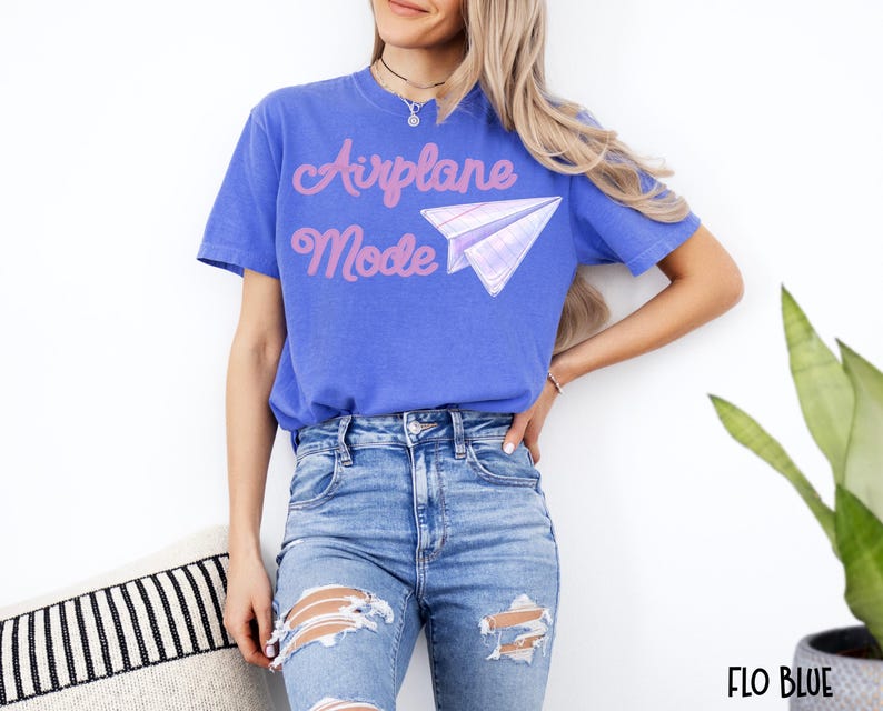 A blue t-shirt with the words "Airplane Mode" in pink script and a paper airplane graphic. The shirt is a solid blue color and is paired with blue jeans.