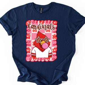 Navy blue t-shirt featuring a cartoon cardinal wearing star-shaped sunglasses and blowing a bubblegum bubble. The graphic is set within a pink and white checkered frame with the word "Cardinals" in a script font.