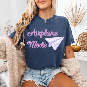 Navy blue t-shirt with the text "Airplane Mode" in a cursive font and a paper airplane graphic. The shirt is made of a soft material and is suitable for casual wear. The word "DENIM" is printed at the bottom left.