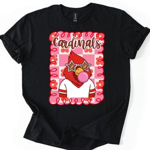 Black t-shirt featuring a cartoon cardinal wearing star-shaped sunglasses and blowing a bubblegum bubble. The design includes the word "Cardinals" in a decorative font, set against a pink and white checkered background.