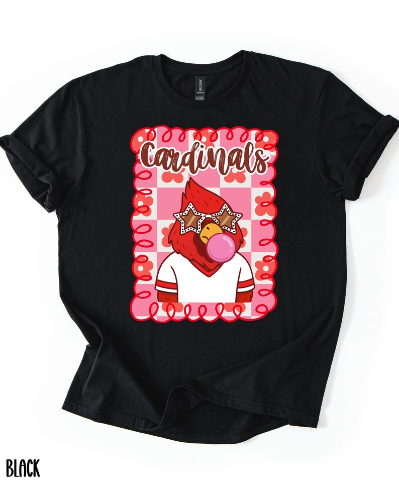 Black t-shirt featuring a cartoon cardinal wearing star-shaped sunglasses and blowing a bubblegum bubble. The design includes the word "Cardinals" in a decorative font, set against a pink and white checkered background.