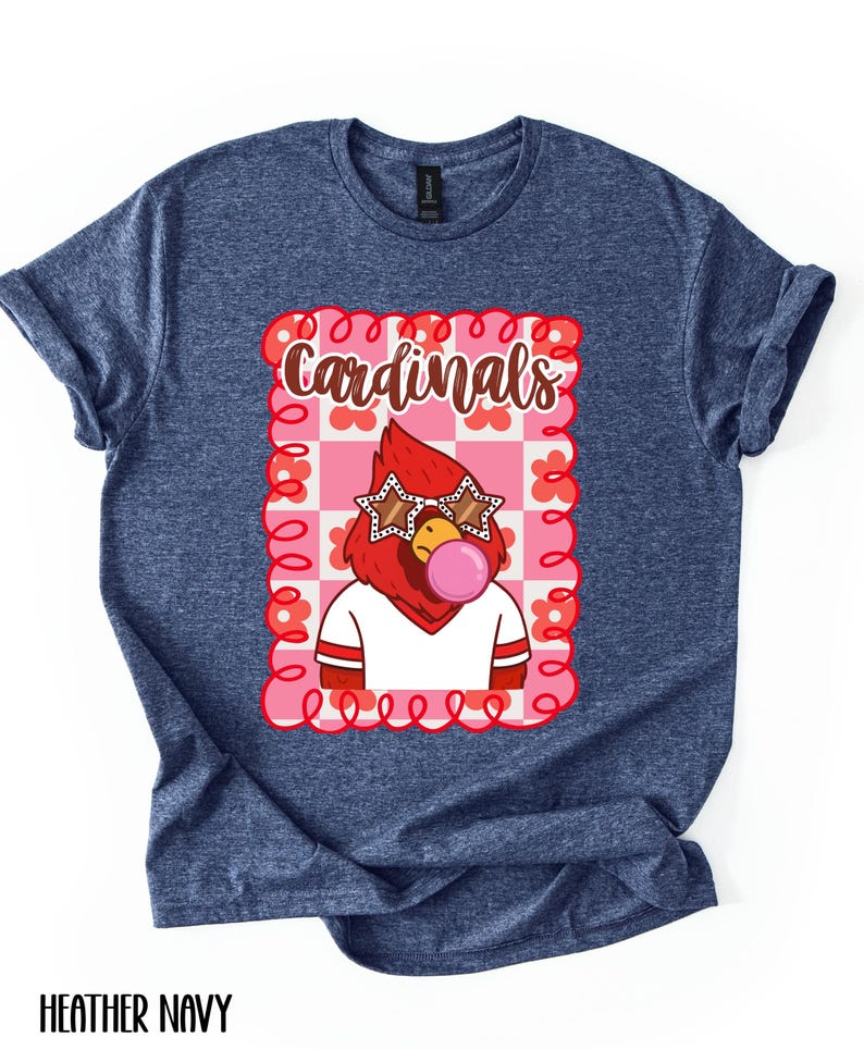 May include: Heather navy blue t-shirt featuring a cartoon cardinal with star-shaped sunglasses blowing a bubblegum bubble. The cardinal is inside a pink and white checkered frame with the word "Cardinals" above it.