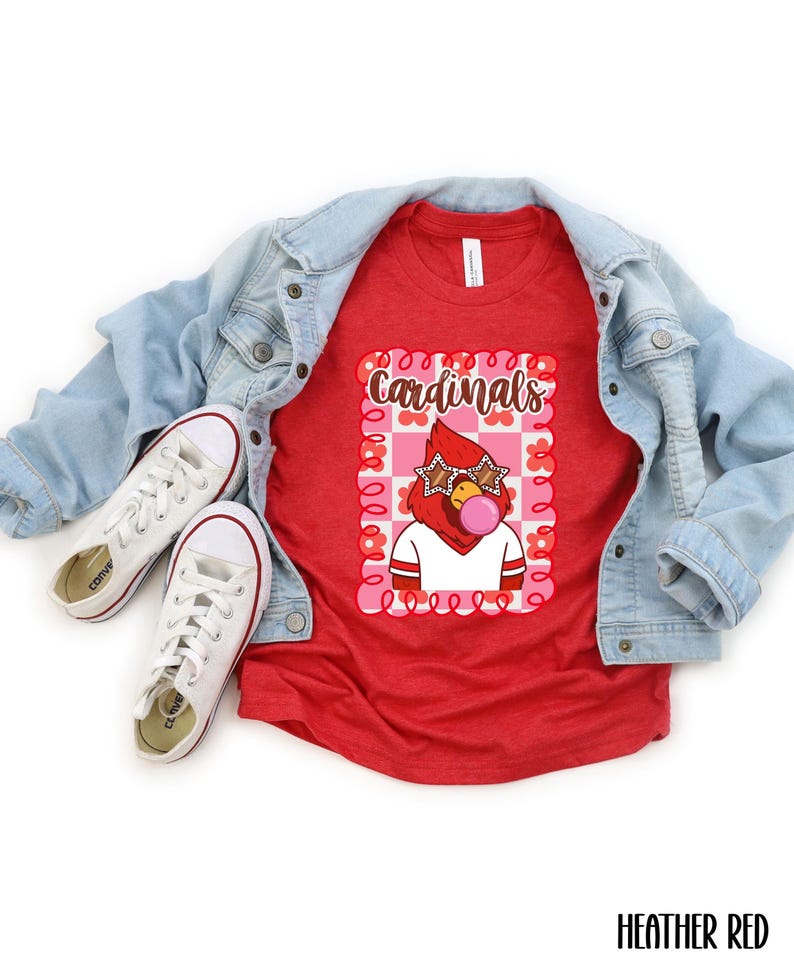 Red t-shirt featuring a cartoon cardinal with star-shaped sunglasses blowing a bubble. The cardinal is wearing a white shirt with red stripes. The word "Cardinals" is written in brown script within a pink and red floral frame.