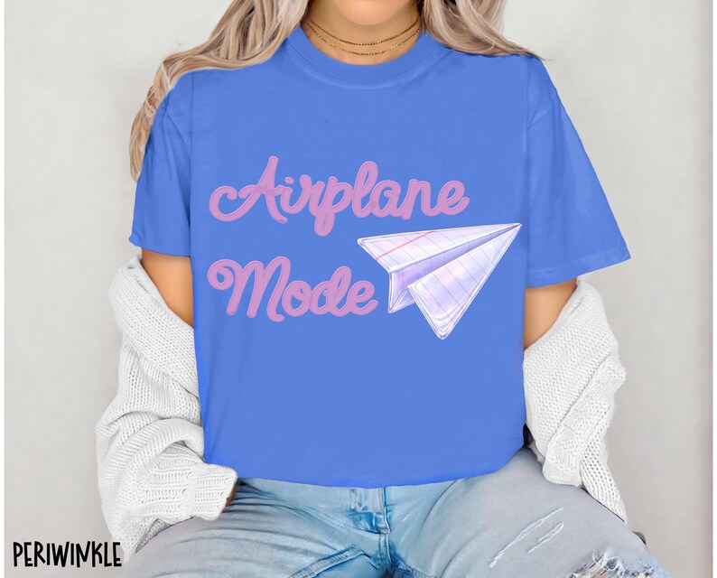 A blue t-shirt with the words "Airplane Mode" in pink script and a paper airplane graphic. The shirt is a solid blue color and has short sleeves.