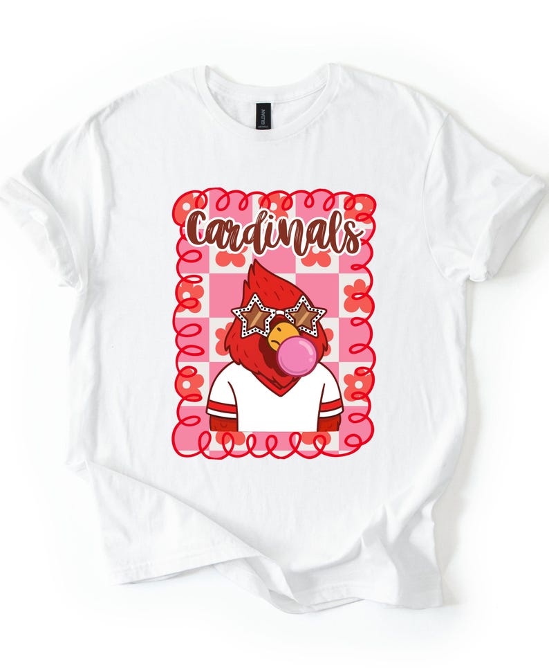 White t-shirt featuring a cartoon cardinal with star-shaped sunglasses blowing a bubble. The cardinal is wearing a white shirt with red stripes. The word "Cardinals" is written in brown script within a pink and red floral frame.
