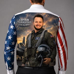 Puede incluir: Una camisa de manga larga con botones y un estampado gráfico en la espalda. El diseño muestra a un piloto con equipo de vuelo sosteniendo un casco, un avión de combate y el texto "CAPTAIN COURAGEOUS STRENGTH IN CHARACTER. COURAGE IN ACTION." Las mangas presentan patrones de la bandera estadounidense.