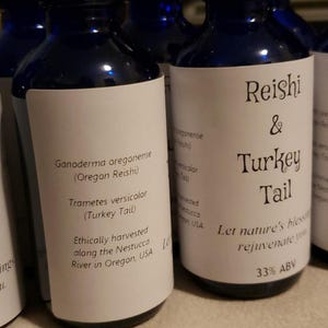 May include: Several dark blue glass bottles with white labels are displayed. The labels feature text including "Reishi & Turkey Tail" and "Ganoderma oregonense". The bottles appear to contain a liquid with a 33% ABV.
