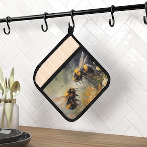 May include: A black and beige oven mitt with a colorful design of two bumblebees flying in front of a floral background.