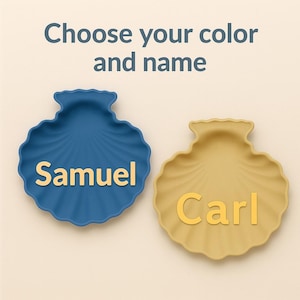 Può includere: Due vassoi a forma di conchiglia, uno blu e uno giallo, ciascuno con un nome in lettere dorate. Il vassoio blu dice "Samuel" e quello giallo dice "Carl". Il testo in alto dice "Scegli il tuo colore e il tuo nome".