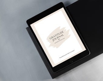May include: A black tablet displaying a gratitude journal cover with the text "Gratitude Journal 2023". The cover has a beige brushstroke design and the text "Good Things, Take Time To Grow". The tablet rests on a black surface.