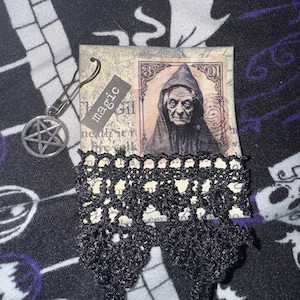 May include: A black and white image of a woman wearing a hooded cloak and a vintage style frame with the word "Magic" written on it. The image is attached to a black crocheted lace trim.