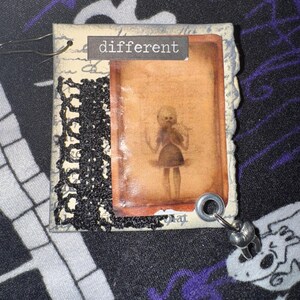 May include: A vintage-style card with a black lace trim and a photo of a doll with the word "different" printed on the front.