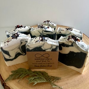 May include: Six bars of handmade soap with a black and white marbled swirl design. The soap is topped with dried flowers and herbs. The soap is labelled "maskihkiwapoy sweet black tea sweet black tea fragrance Three Sisters Soap".