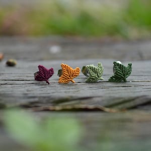 Peut inclure: Quatre boucles d'oreilles à tige en forme de feuilles, chacune fabriquée à partir de fil noué. L'ensemble comprend une feuille bordeaux foncé, une feuille jaune doré, une feuille vert sauge clair et une feuille vert forêt foncé.