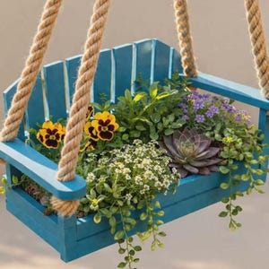 May include: A hanging planter shaped like a blue Adirondack chair, filled with a variety of colorful flowers and greenery. The planter is suspended by thick, natural-colored ropes, creating a charming, rustic aesthetic.