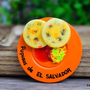 🫓🔥 Magneto de Pupusas – Sabor y Tradición Salvadoreña 🇸🇻

Decora tu hogar con este magneto artesanal de pupusas, hecho en porcelana fría con detalles realistas que capturan la esencia del platillo más icónico de El Salvador. 🌟 Su diseño recrea el dorado perfecto de una pupusa recién hecha, evocando su delicioso aroma y sabor casero. Ideal para coleccionistas y amantes de la cultura salvadoreña.