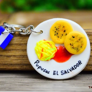 🫓🔥 **Llavero de Pupusas – Tradición Salvadoreña** 🇸🇻  

Lleva contigo el sabor de **El Salvador** con este **llavero artesanal de pupusas**, elaborado en **porcelana fría** con detalles realistas. Su diseño recrea el dorado perfecto de una pupusa recién salida de la **plancha**, capturando su esencia única. **Duradero, resistente y perfecto para coleccionistas y amantes de la comida típica.** Un símbolo de orgullo salvadoreño que te conecta con tus raíces.