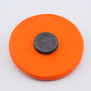 Puede incluir: Un disco de cer&aacute;mica naranja brillante con un centro circular negro. El disco es liso y tiene una superficie ligeramente texturizada.