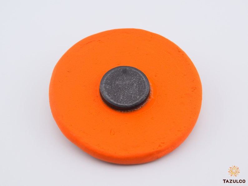 Puede incluir: Un disco de cer&aacute;mica naranja brillante con un centro circular negro. El disco es liso y tiene una superficie ligeramente texturizada.