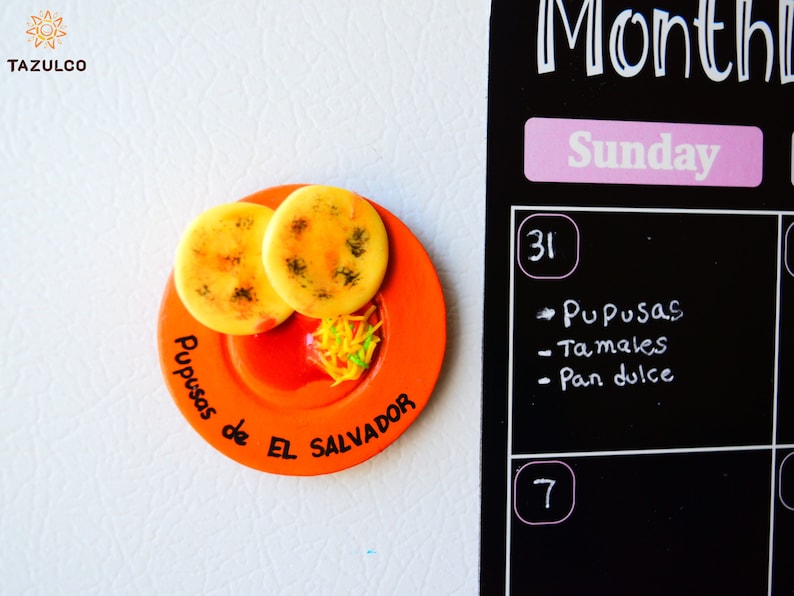 Puede incluir: Un plato de cer&aacute;mica naranja con dos pupusas amarillas y salsa roja. El plato tiene el texto "Pupusas de El Salvador" escrito en &eacute;l.